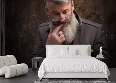 Portrait of a gray-haired bearded man with glasses reading book in Russian, on the cover Russian inscription M. Gorky, selective focus Wall mural