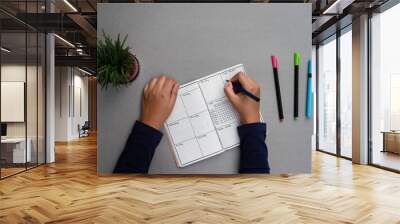 Setting up a bullet journal for mental well being and personal development. Weekly planner set up on a minimal grey table top, with sketch pens and a green house plant Wall mural