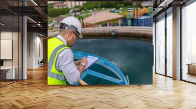 environmental engineer working at the wastewater treatment try to check the quality of the water in a tank and write donw the test result on a clipboard Wall mural