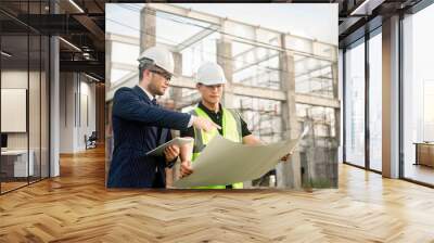 Two construction engineers are discussing about building construction plans at a construction site. Wall mural