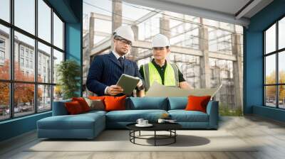 Two construction engineers are discussing about building construction plans at a construction site. Wall mural