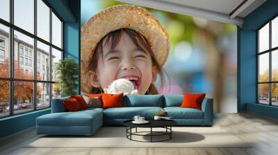 Thai girl happily eats ice cream, She wears a straw hat and smiles while licking her lips. Her mouth was covered in white condensation from eating an ice cream cone Wall mural