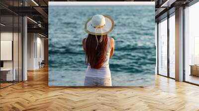 Young woman in summer outfit and hat by seaside Wall mural