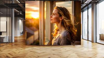 woman gazes thoughtfully out window at beautiful sunset Wall mural