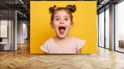 portrait of a happy excited little girl with an amazed look and open mouth on a yellow background Wall mural