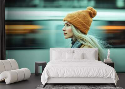 young woman with long blonde hair in a beanie and a coat standing on a train plattform Wall mural