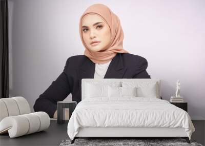 A beauty shot of a pretty young Asian hijab corporate girl with smooth glowing skin smiling and relaxing on a table over white background studio. Beauty skin care, office concept. Wall mural