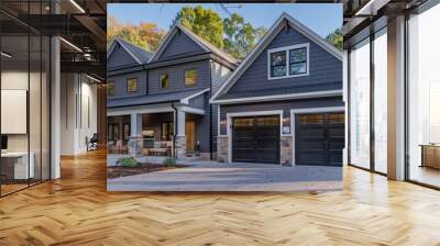 The fresh look of a new construction home with contemporary gray siding, stone columns, and a pair of garages, the front porch adorned with modern furniture at noon Wall mural