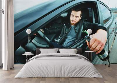 A drunken man driving a car with a bottle of alcohol in his hand.A man holds a driving wheel and a bottle of beer Wall mural