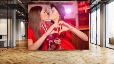 Two young lesbian girls kiss and make a heart with their hands at a club party Wall mural