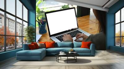 Behind view of a young woman using a white blank screen computer laptop at the wooden working desk. Wall mural