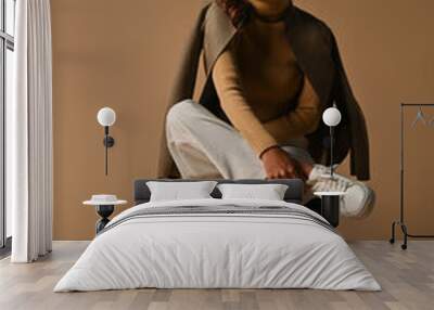 Full body portrait of Young Asian woman in cross legged pose on chair. taken at the studio on a brown background. Wall mural