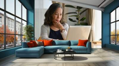 Old woman work at home using notebook computer. Wall mural