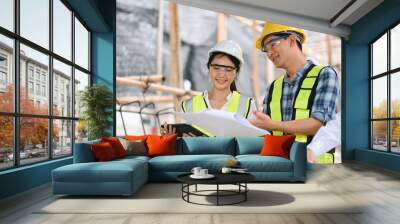 Two construction professionals in safety gear review and discuss project details on blueprint and tablet at a construction site Wall mural