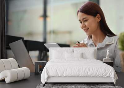 Young millennial businesswoman in casual outfit working with laptop and tablet in co working space. Wall mural