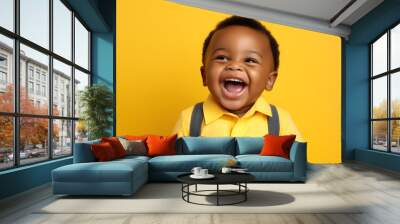 Portrait of a cute African American baby boy wearing yellow shirt with braces laughing on bright yellow background Wall mural