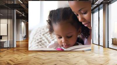 Preschool age black girl sitting with her mother reading a story book Wall mural