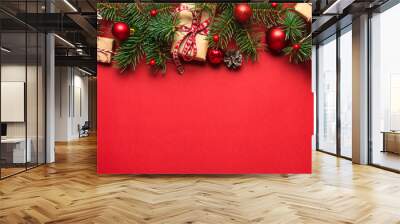 Christmas composition made of fir branches, gift boxes, red holiday decorations on red background Wall mural