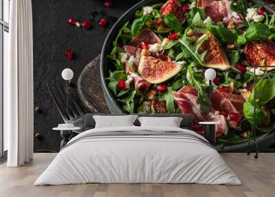 Salad with figs, goat cheese, prosciutto, rucola, nuts and pomegranate with fork on black background. close up Wall mural