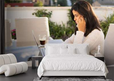 Shallow focus of a Middle Eastern female talking on the phone while using her laptop at a cafe Wall mural