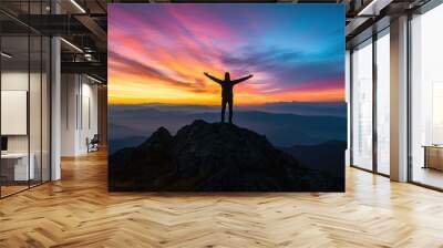 Silhouette of a person with arms outstretched towards the sky, standing on a mountain peak at sunrise, symbolizing freedom. Wall mural