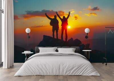 Two people silhouette with arms raised up on mountain top at sunset Wall mural