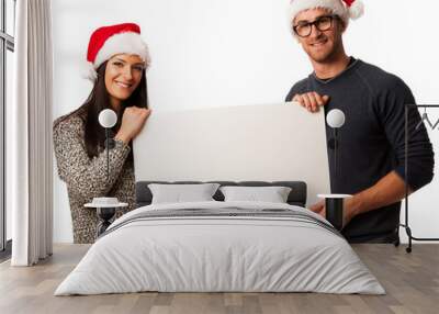 Young couple in santa hats holding blank board for advertisement Wall mural