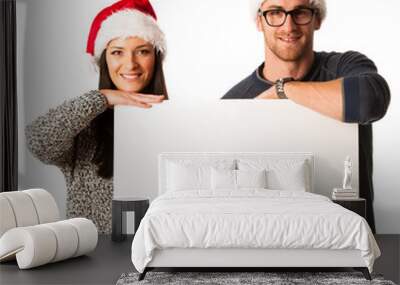 Young couple in santa hats holding blank board for advertisment. Wall mural