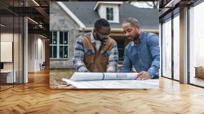 Two men reviewing construction blueprints on site, discussing architectural plans in front of a partially constructed house. Wall mural