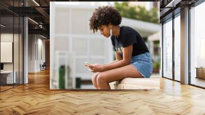 Outdoor portrait of a Young black African American young woman texting  on mobile phone Wall mural