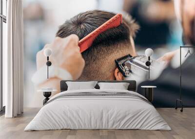 Barber cutting the hair of an adult male with a shaving machine and ca comb Wall mural