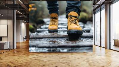 Closeup of a person's feet wearing yellow boots walking on a wooden bridge over a stream in the forest. Wall mural