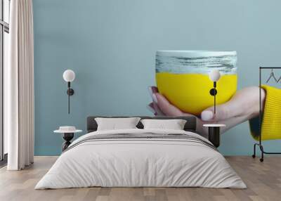 compact artistic coffee cup with craggy stratified texture in vibrant yellow and grey creative silhouette female model's hands cradling the cup in minimalist pose clean white background studio Wall mural