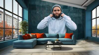 City portrait of handsome hipster guy with beard wearing gray blank hoodie or hoody and hat with space for your logo or design. Mockup for print Wall mural