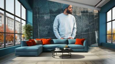 City portrait of handsome hipster guy with beard wearing gray blank hoodie or hoody and hat with space for your logo or design. Mockup for print Wall mural