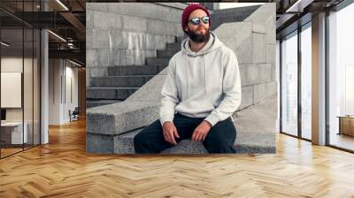 City portrait of handsome hipster guy with beard wearing gray blank hoodie or hoody with space for your logo or design. Mockup for print Wall mural