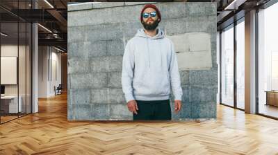 City portrait of handsome hipster guy with beard wearing gray blank hoodie or hoody with space for your logo or design. Mockup for print Wall mural