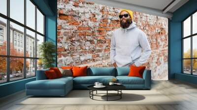 City portrait of handsome hipster guy with beard wearing gray blank hoodie or sweatshirt and hat with space for your logo or design. Mockup for print Wall mural