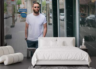 Handsome hipster man in sunglasses walking along the street. White t-shirt. Wall mural