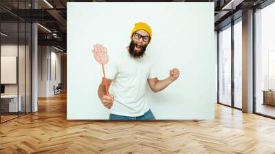 Young caucasian hipster man holding a fly swatter wanting to kill annoying mosquito or a fly. Wall mural