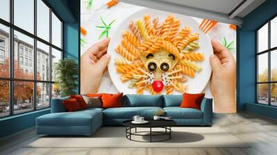 Fun food idea for kids lunch, animal shaped food art - colorful fusilli vegetables pasta with sandwich like a cute lion head on white plate top view Wall mural