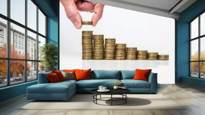 Hand laying yellow coins on stacks of yellow coins in a row on a white background Wall mural