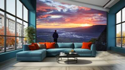 Man standing on a ledge of a mountain, enjoying the beautiful sunset over a wide river valley in Thorsmork, Iceland.
 Wall mural