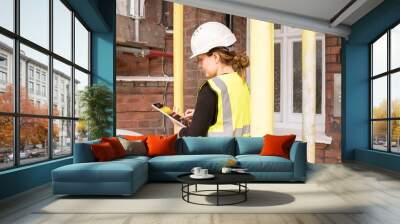 Female civil engineer taking notes on her tablet with electronic pen during a survey, hard hat and yellow high visibility vest, supervision and inspection, technology and innovation in construction Wall mural