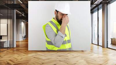 Bearded man architect wearing safety helmet and reflective jacket tired rubbing nose and eyes feeling fatigue and headache. Stress and frustration concept. Wall mural