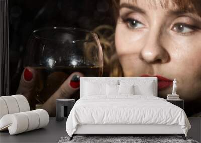 mysterious young woman with a glass of wine posing behind transparent glass covered by water drops. on a dark background Wall mural