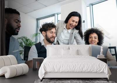 A team of professionals working on a project together in the office. They are looking at the laptop, satisfied with what they have so far. Wall mural