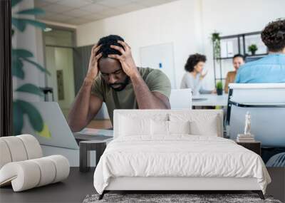 A young man stuck with a problem at work, holding his head and thinking hard. Wall mural