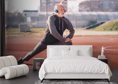 An older man stretching his legs at the basketball court wearing headphones.sportsperson Wall mural