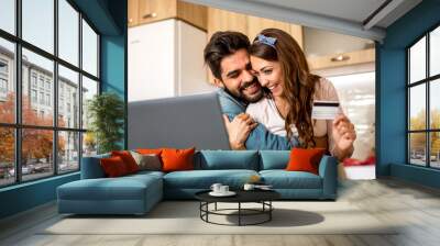 Beautiful young Caucasian couple in love embracing, happy with their first mutual online purchase on laptop in the kitchen. Wall mural